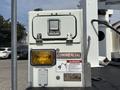 A white utility box with a yellow light and a commercial label mounted on a truck's platform with warning and operational stickers