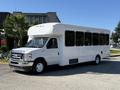 A white 2021 Ford Econoline bus with large side windows and a sleek profile parked on a street