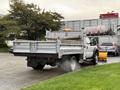 A 2013 Ford F-450 SD truck with a flatbed and a plow attachment on the front is parked, emitting a light mist from the engine area
