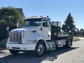 A 2020 Peterbilt 330 flatbed truck with a chrome grille and orange lights on the roof parked at an angle with visible wheels and a side-mounted metal rack