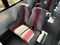 Two gray bus seats with red stripes and seatbelts arranged in a row inside a vehicle