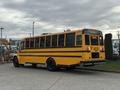 A yellow 2022 Freightliner B2 school bus with black wheels parked at the side of a lot