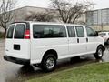 A white 2021 Chevrolet Express van with sliding doors and chrome wheels parked on a wet surface