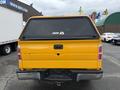 A yellow 2014 Ford F-150 with a black hardtop cover on the bed and a rear view showing the tailgate and back lights