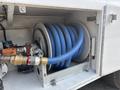 A compartment of a 2010 Freightliner M2 106 displaying a large reel with blue hose coiled around it alongside metal fittings and a motor assembly