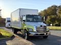 A 2018 Hino 268 box truck with a white cargo compartment and green accents parked on a street