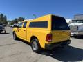 A bright yellow 2015 RAM 1500 pickup truck with a canopy in the bed and chrome wheels parked at a location