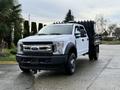 A white 2017 Ford F-450 Super Duty pickup truck with a flatbed and black rear cargo area parked on a wet surface