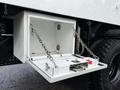 A white storage compartment with chains is attached to the side of a 2015 Freightliner M2 truck with a pullout tray for storage and a wheel for mobility