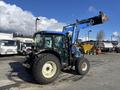 A blue 2010 New Holland T4050 tractor with a loader attachment parked at a dealership surrounded by various vehicles and equipment.