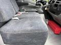 The interior of a 2018 Hino 195 featuring a gray fabric driver's seat with patterned upholstery and a red toolbox visible on the floor near the front console