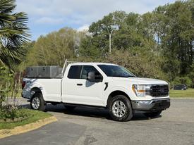 A white 2021 Ford F-150 pickup truck with a single cab and a tool box in the truck bed parked on a smooth surface