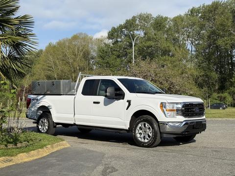 A white 2021 Ford F-150 pickup truck with a single cab and a tool box in the truck bed parked on a smooth surface