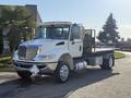 A 2017 International 4300 flatbed truck in white with chrome accents and a black cargo area, featuring a diamond-shaped emblem on the front grille