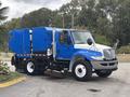 A blue 2013 International DuraStar 4300 street sweeper truck with a front broom attachment and a large storage compartment on the back