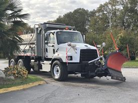 A white 2013 Freightliner 114SD truck equipped with a snow plow and salter attached to its rear