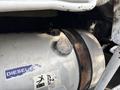 A large silver diesel tank with a rounded cap and visible wear marks, featuring a blue label that reads "DIESEL" and an instruction sticker for handling