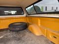 A 2014 Ford F-150 truck bed with an orange interior and a spare tire resting against the side