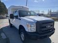 A 2016 Ford F-250 Super Duty pickup truck in white with a large cab shell on the bed and black front grille parked with one door open