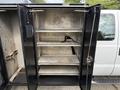 A black enclosed storage unit with multiple shelves designed for a 2008 Ford F-450 SD with open double doors showing the interior compartments