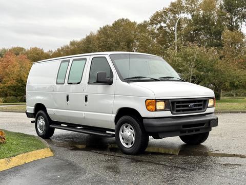 A white 2006 Ford Econoline van with a boxy shape and sliding side doors parked on a wet surface