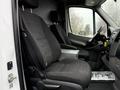 Two black fabric front seats of a 2017 Mercedes-Benz Sprinter with a center console between them and dashboard controls visible