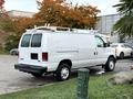 A white 2008 Ford Econoline van with roof racks parked at a location with trees in the background
