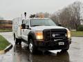 A 2015 Ford F-450 with a white body and utility box attached at the back featuring a black front grille and multiple orange light bars on the roof
