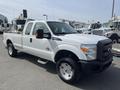A 2014 Ford F-250 Super Duty pickup truck with a white exterior and silver wheels parked in a lot