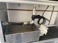 A metal tank with attached piping and valves inside a compartment with electrical wiring and a white cloth on the bottom