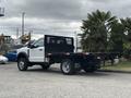 A white 2023 Ford F-450 Super Duty with a flatbed and black mesh sides, showcasing the vehicle's sturdy design and heavy-duty capabilities