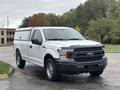 A white 2020 Ford F-150 pickup truck with a black grille and silver wheels is parked in a lot with a truck bed cap