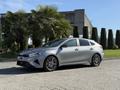 A silver 2024 Kia Forte5 with sporty features and sleek lines parked on a paved area with greenery in the background