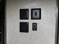 Four black switch plates installed on a fabric-covered wall, arranged in a grid pattern, with one plate slightly smaller than the others