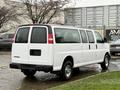 A white 2021 Chevrolet Express van with a long body and multiple side windows parked at an angle with visible rear doors and chrome wheels