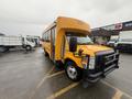 A yellow 2021 Ford Econoline bus with a large front grille and safety features parked at an angle with a clear view of its front side and tires