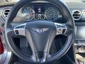 A close-up view of the steering wheel of a 2015 Bentley Continental GT featuring the Bentley logo and multiple dashboard gauges in the background