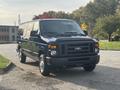 A 2013 Ford E-350 Super Duty van with a dark blue exterior parked on an outdoor surface showcasing its large wheel design and front grille
