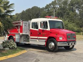 A red 1999 Freightliner FL80 fire truck with a silver chassis and emergency lights on top parked at an angle with a fire hose compartment on the side