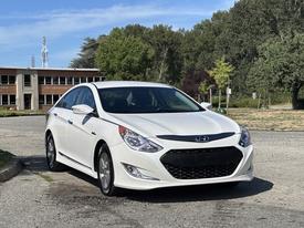 A white 2015 Hyundai Sonata with sleek lines and a modern design parked at a location with green trees in the background