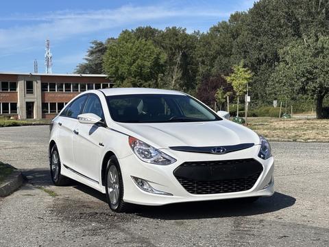 A white 2015 Hyundai Sonata with sleek lines and a modern design parked at a location with green trees in the background