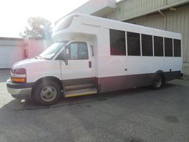 A white 2020 Chevrolet Express shuttle bus with black trim and large windows on the side parked at a facility