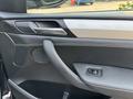 Interior door panel of a 2013 BMW X3 featuring a modern design with a silver handle and speaker area. The texture is primarily black leather with light stitching
