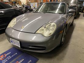 A silver 2003 Porsche 911 sports car with distinctive round headlights and a sleek design parked inside a garage