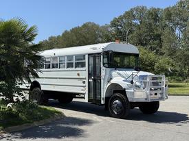 A white 2009 International 3000 CE school bus with large windows and a reinforced front grill parked on a street