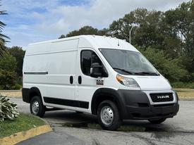 A 2021 RAM Promaster van with a white exterior and sliding side door parked on a slight incline