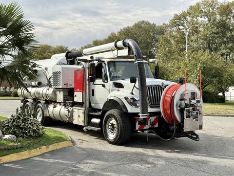 A white 2014 International 7500 truck with a large tank and equipment mounted on its side featuring a red hose reel and various attachments