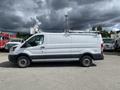 A white 2019 Ford Transit van with a gray lower strip and roof racks visible on top parked in a lot