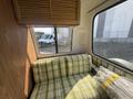 Interior view of a 1976 GMC Motorhome featuring a plaid green and yellow couch and wooden storage cabinets