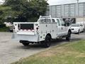 A white 2013 Ford F-250 SD with a utility bed and ladder rack is parked, featuring storage compartments on the sides and a flatbed at the rear